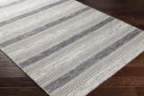 Close-up of Vernonia Area Rug. Black and ivory wool rug with a striped, geometric pattern on dark wood floors. Corner