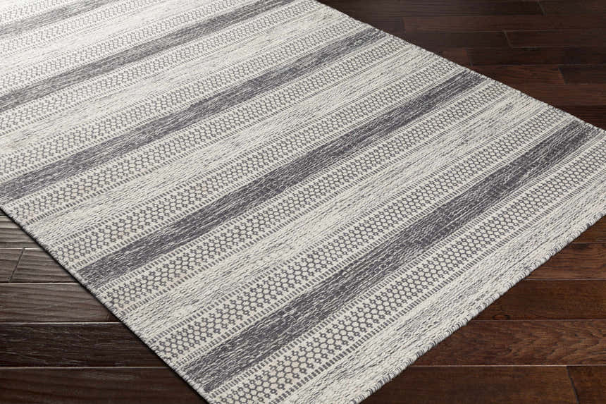 Close-up of Vernonia Area Rug. Black and ivory wool rug with a striped, geometric pattern on dark wood floors. Corner