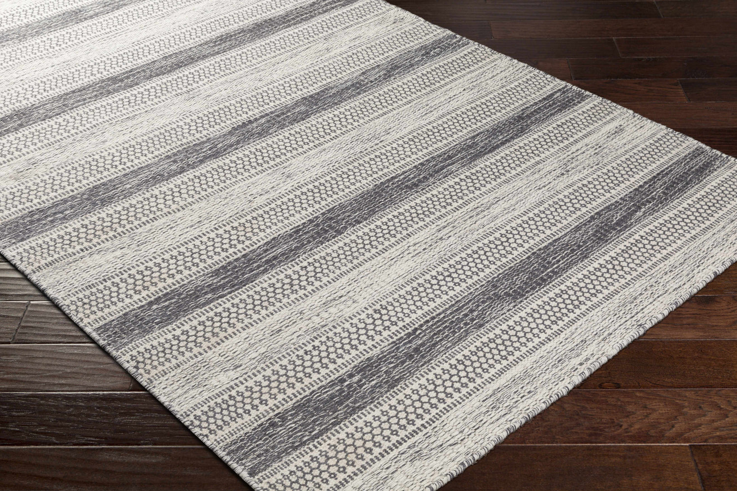 Close-up of Vernonia Area Rug. Black and ivory wool rug with a striped, geometric pattern on dark wood floors. Corner