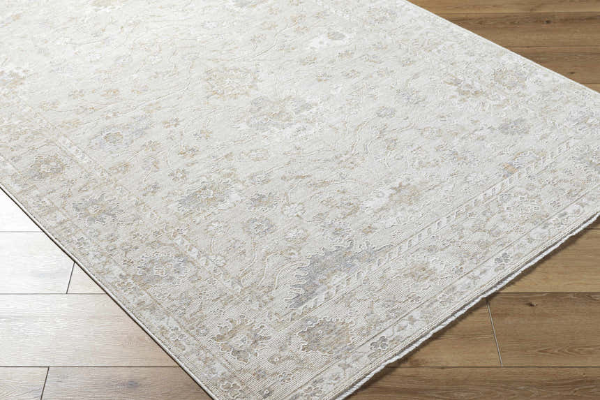 Close-up of the Vaman Luxe Rug in light silver and sterling gray with a traditional floral pattern on wood floors. Corner