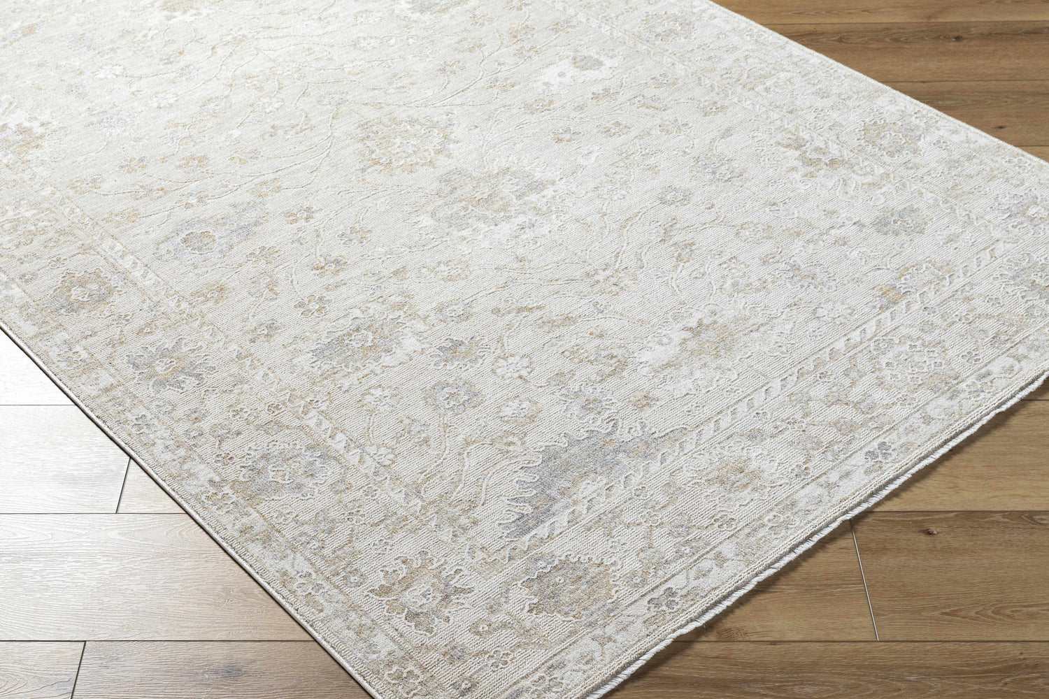 Close-up of the Vaman Luxe Rug in light silver and sterling gray with a traditional floral pattern on wood floors. Corner