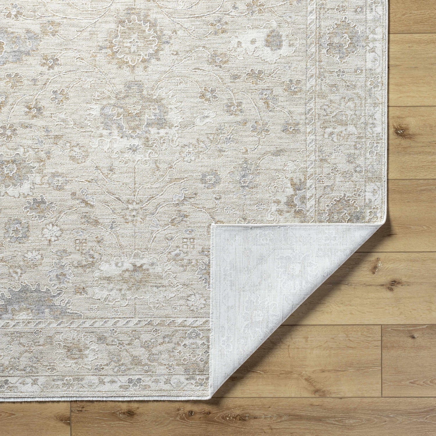 Close-up of the Vaman Luxe Rug showing its light silver and sterling gray traditional floral pattern and machine-woven texture. Fold