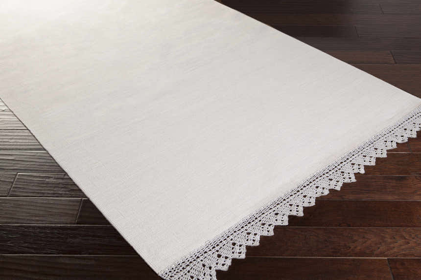 Close-up of the hand-woven Grace GRC-7003 area rug, showing its cotton texture and delicate crochet trim on dark wood floors. Corner