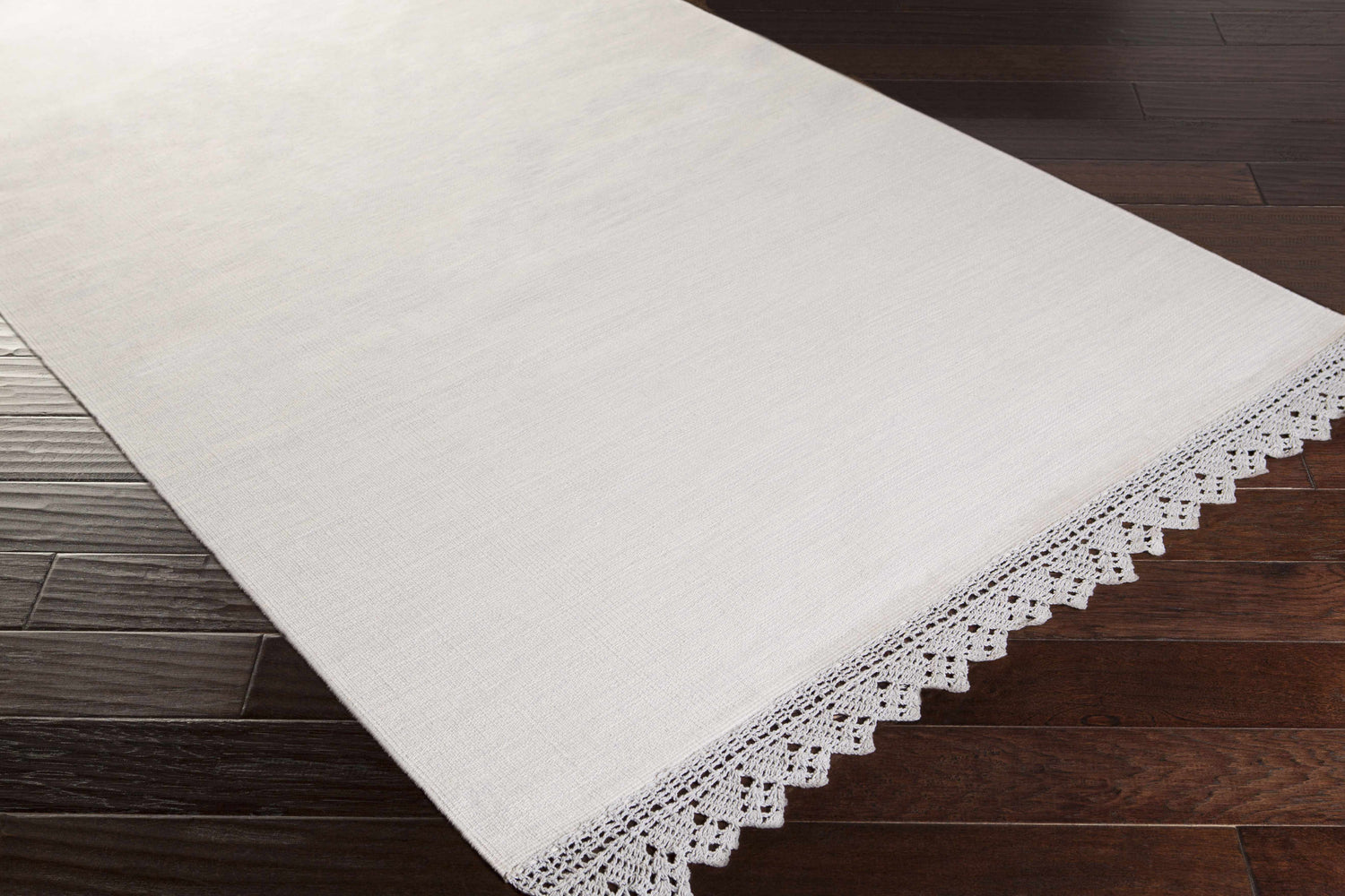 Close-up of the hand-woven Grace GRC-7003 area rug, showing its cotton texture and delicate crochet trim on dark wood floors. Corner