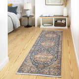 Bedroom scene with a Wailua Area Rug runner in blue, beige, and rust colors on wood floors. Bed and bench visible. Roomscene-Runner