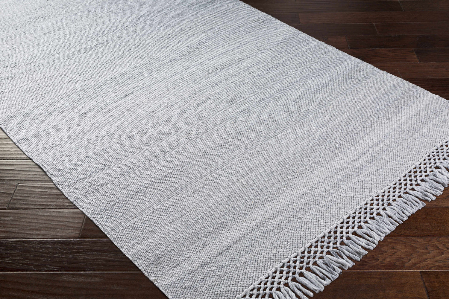 Close-up of the light gray Walcha Indoor & Outdoor Rug with fringe on dark wood floors. Hand woven texture. Corner