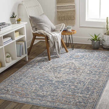 Cozy reading nook with a Buguey Cream&Blue area rug, white shelving, and a woven chair with a throw. Roomscene-Rectangle
