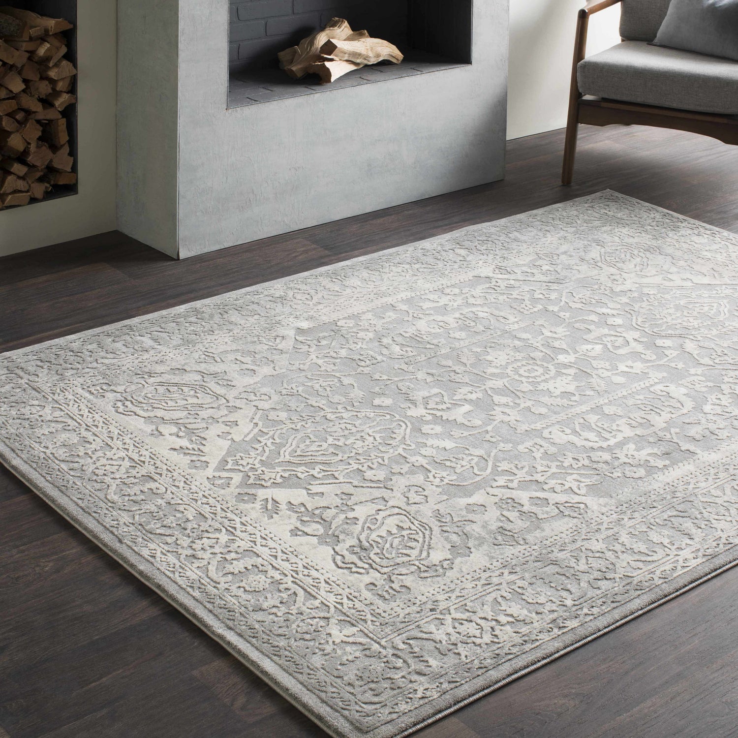 Living room scene with a gray Watford Updated Traditional Tibetan Rug, fireplace, dark wood floors, and gray chair. Roomscene-Rectangle