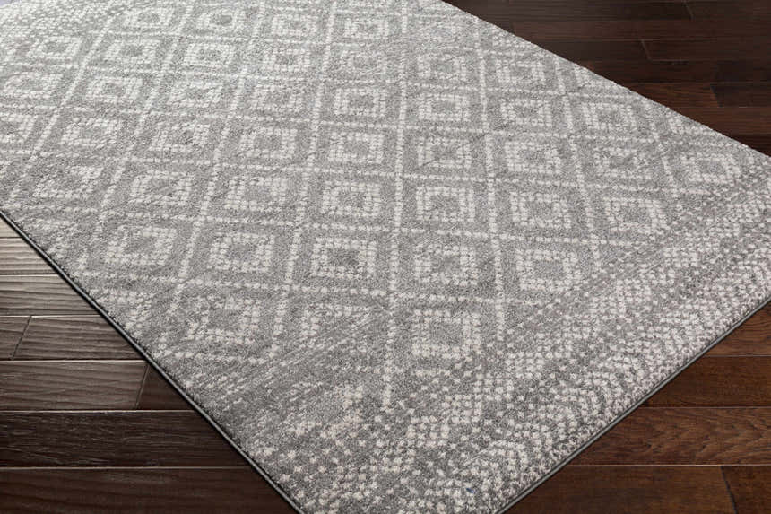 Close-up of the Webb Area Rug, showcasing its charcoal, gray, and white geometric pattern and soft texture on dark wood floors. Corner