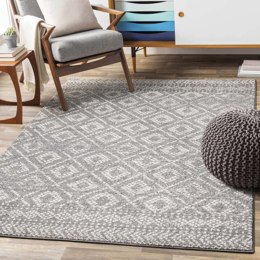 Living room scene with gray armchair, pouf, and geometric Webb Area Rug in charcoal, gray, and white. Roomscene-Rectangle