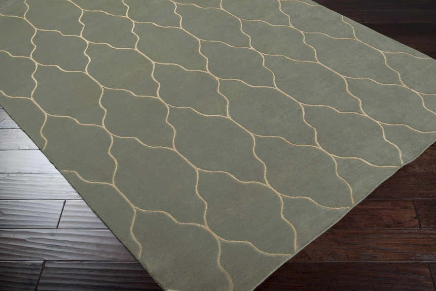 Close-up of the Woodland Area Carpet. Hand-knotted wool rug in muted green with a beige geometric trellis pattern. Corner