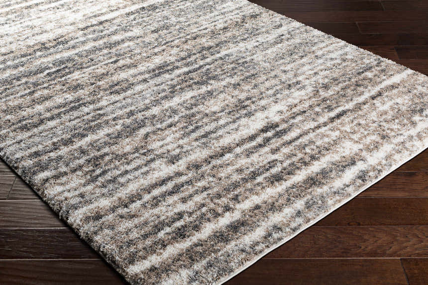 Close-up of a Weddin Striped Plush Area Rug. Charcoal, cream, gray, and tan stripes on a soft, textured shag rug. Corner