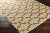 Close-up of the Weehawken Area Rug. Ivory rug with a bright orange quatrefoil pattern on dark wood floors. Corner