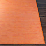 Close-up of the orange Weobley Area Rug showing the texture and woven pattern. Polypropylene rug on dark wood floor. Front