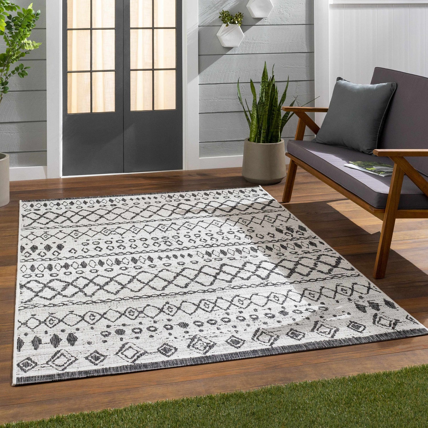 Outdoor patio scene with a black and white Westside Outdoor Area Rug, wooden bench, and potted plants. Roomscene-Rectangle