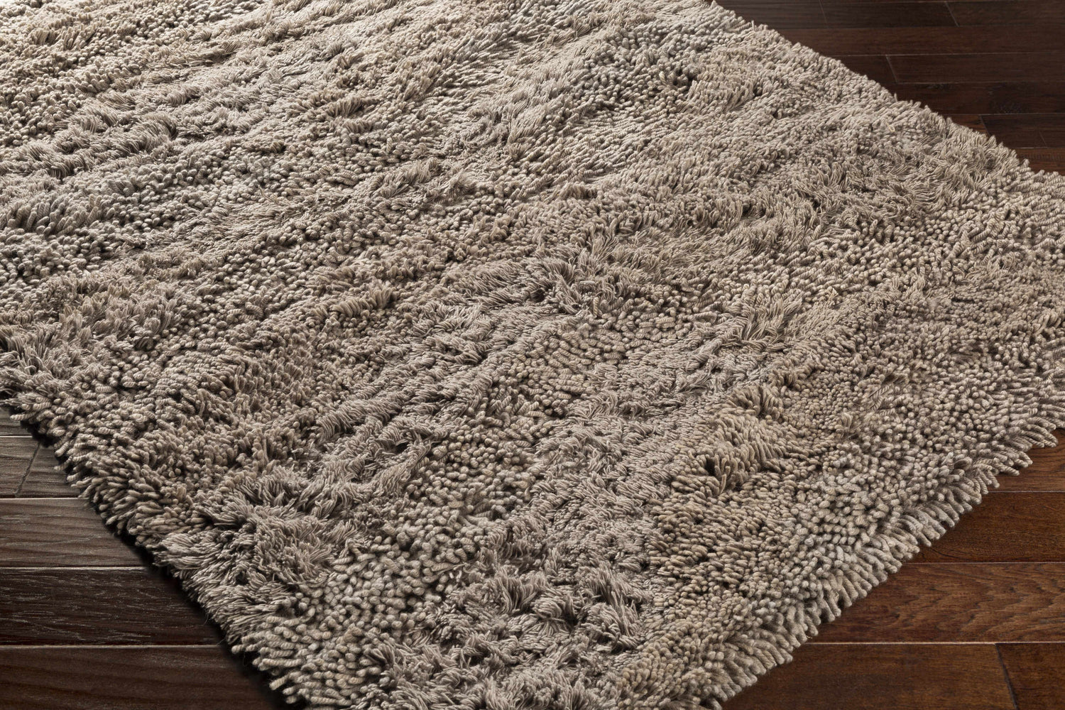 Close up of a textured, hand woven Wharton Carpet in neutral tones on a dark wood floor. Corner