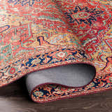 Close-up of the rolled-up Whittingham Area Rug showing its brick red, cream, and navy Oriental-style pattern. Fold