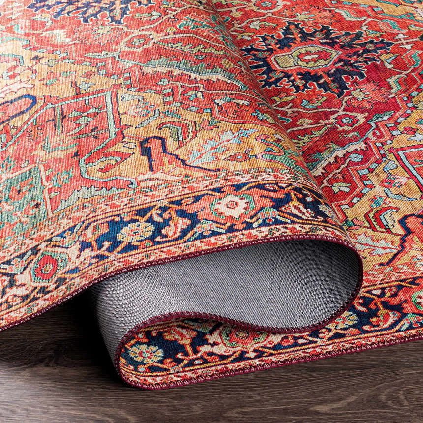 Close-up of the rolled-up Whittingham Area Rug showing its brick red, cream, and navy Oriental-style pattern. Fold