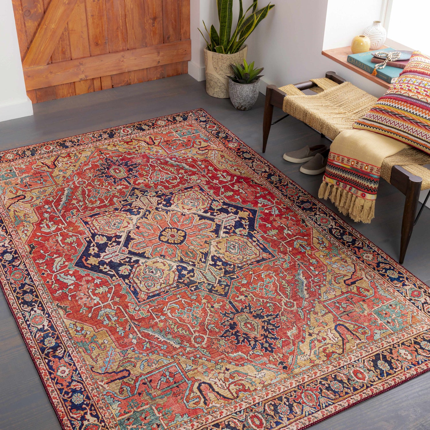 Entryway with a brick red and navy Whittingham Area Rug, woven bench, wood door, and plants. Roomscene-Rectangle