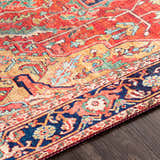 Close-up of the Whittingham Area Rug showing its brick red, cream, and navy bohemian pattern on dark wood flooring. Texture