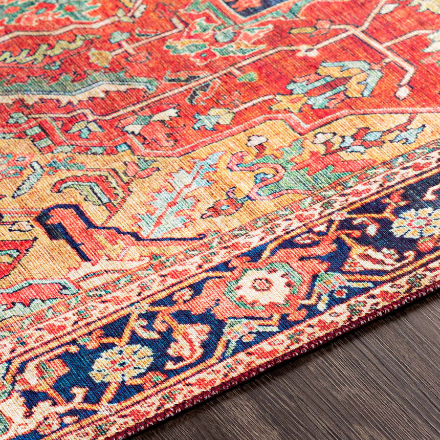 Close-up of the Whittingham Area Rug showing its brick red, cream, and navy bohemian pattern on dark wood flooring. Texture