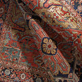 Close-up of the Whittingham Area Rug, a traditional rug in brick red, cream, navy, and brown with an ornate oriental pattern. Fold