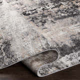 Close-up of the Witchford Abstract Charcoal Thick Rug showing its texture, colors (black, gray, ivory, tan) and machine-woven construction. Fold