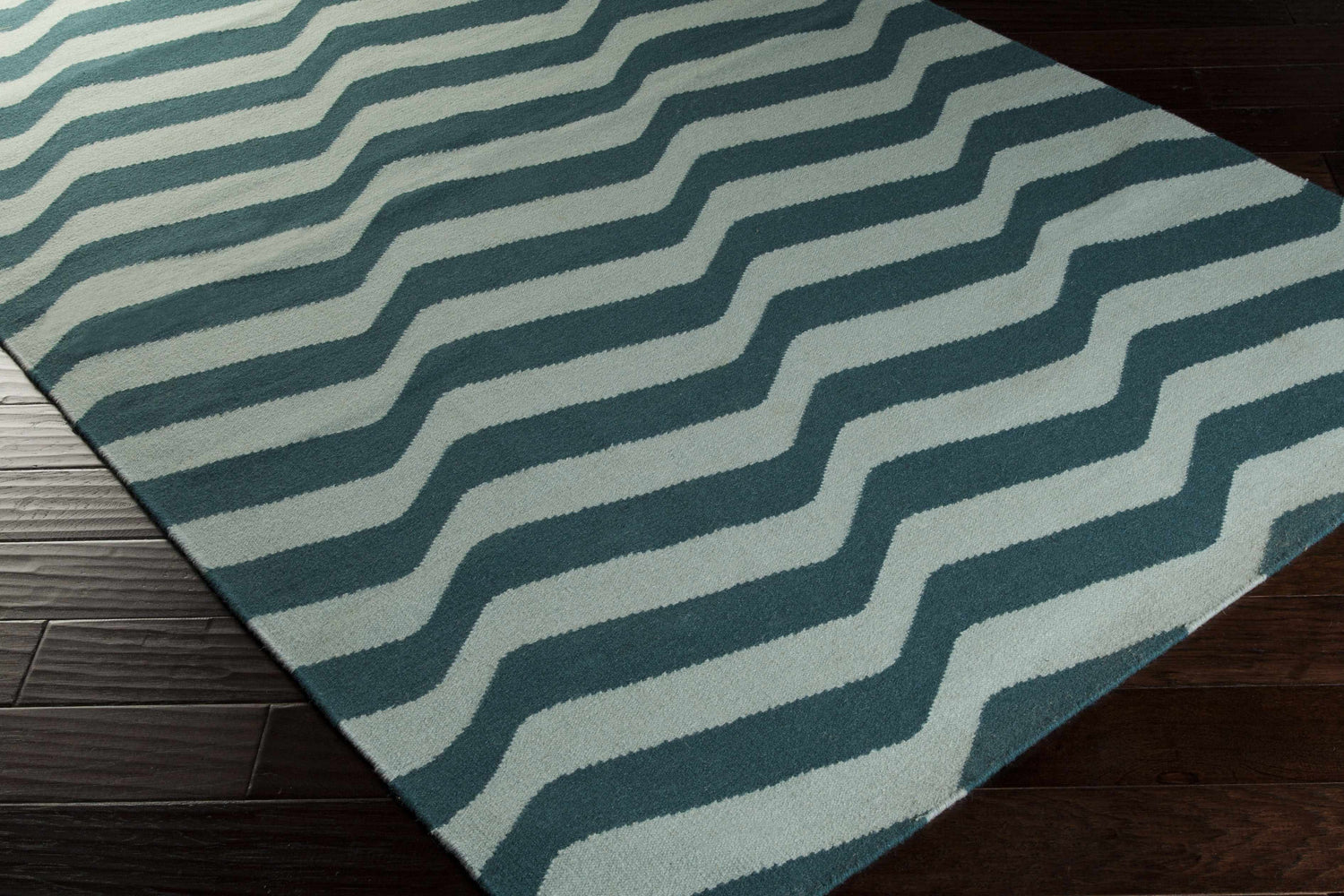 Close-up of the Willis Area Rug. Hand-woven wool rug in dusty sage and teal wavy stripes on dark wood floor. Corner