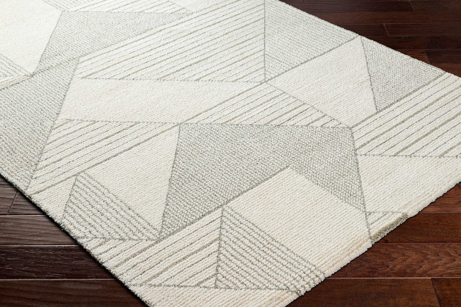 Close-up of the Wald Area Rug showing its beige and gray geometric pattern and textured weave on a dark wood floor. Corner