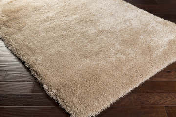 Close-up of the solid tan Woodridge shag area rug showing its plush texture against dark wood floors. Corner
