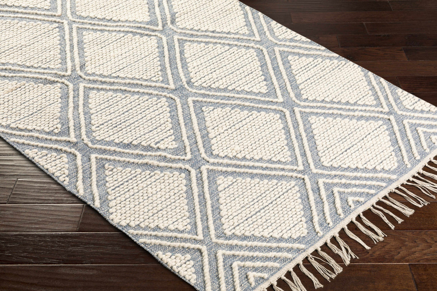 Close-up of the Wausa Denim Trellis on Cream rug, showing geometric diamond pattern and fringe detail on dark wood floor. Corner