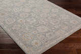 Close-up of the Wurtulla Thick Luxe Statement Rug. The rug has a traditional floral pattern and colors of dusty sage, beige, and brown. Corner