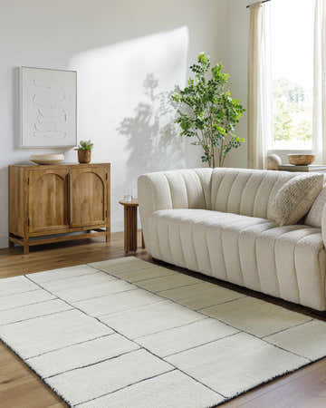 Living room scene with a pearl Xylia Ivory Area Rug, wood cabinet, and textured white sofa. Contemporary style. Roomscene-Rectangle