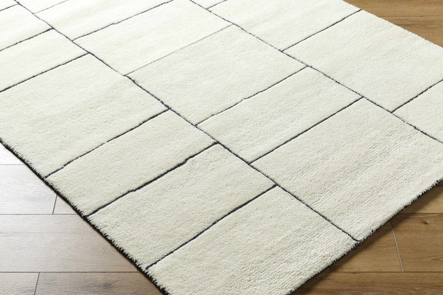 Close-up of a hand-tufted Xylia Ivory Area Rug. The pearl-colored wool rug has a contemporary geometric pattern. Corner