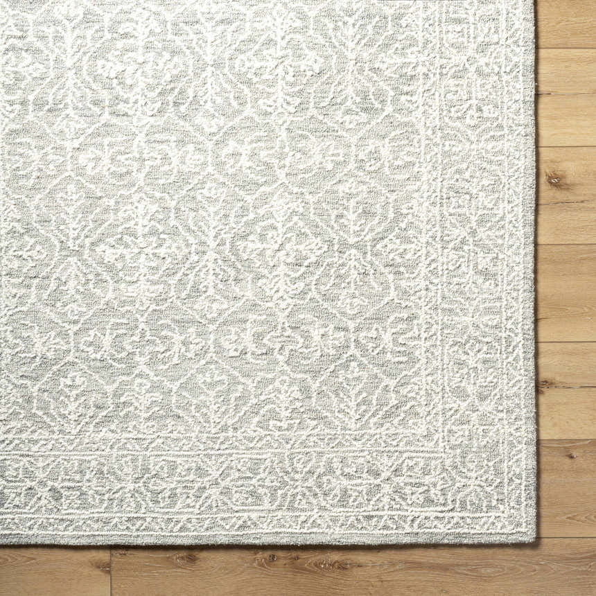 Close-up of the hand-tufted Yadid Gray Wool Area Rug featuring a traditional light silver and gray floral pattern. Corner