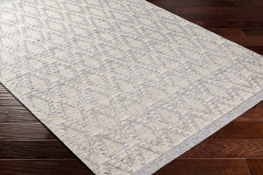 Close-up of the hand woven Yank Area Rug. Light gray and dark gray geometric pattern on a textured rug. Corner