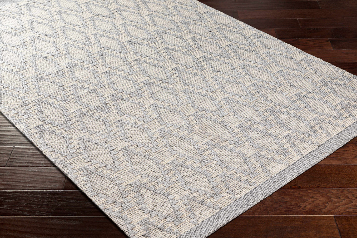 Close-up of the hand woven Yank Area Rug. Light gray and dark gray geometric pattern on a textured rug. Corner