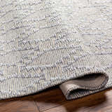 Close-up of the hand-woven Yank Area Rug. Features a gray geometric pattern and textured design. Fold