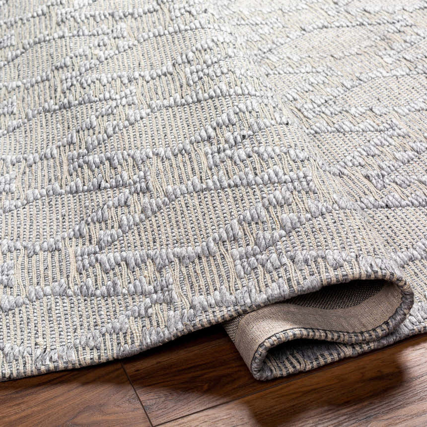 Close-up of the hand-woven Yank Area Rug. Features a gray geometric pattern and textured design. Fold