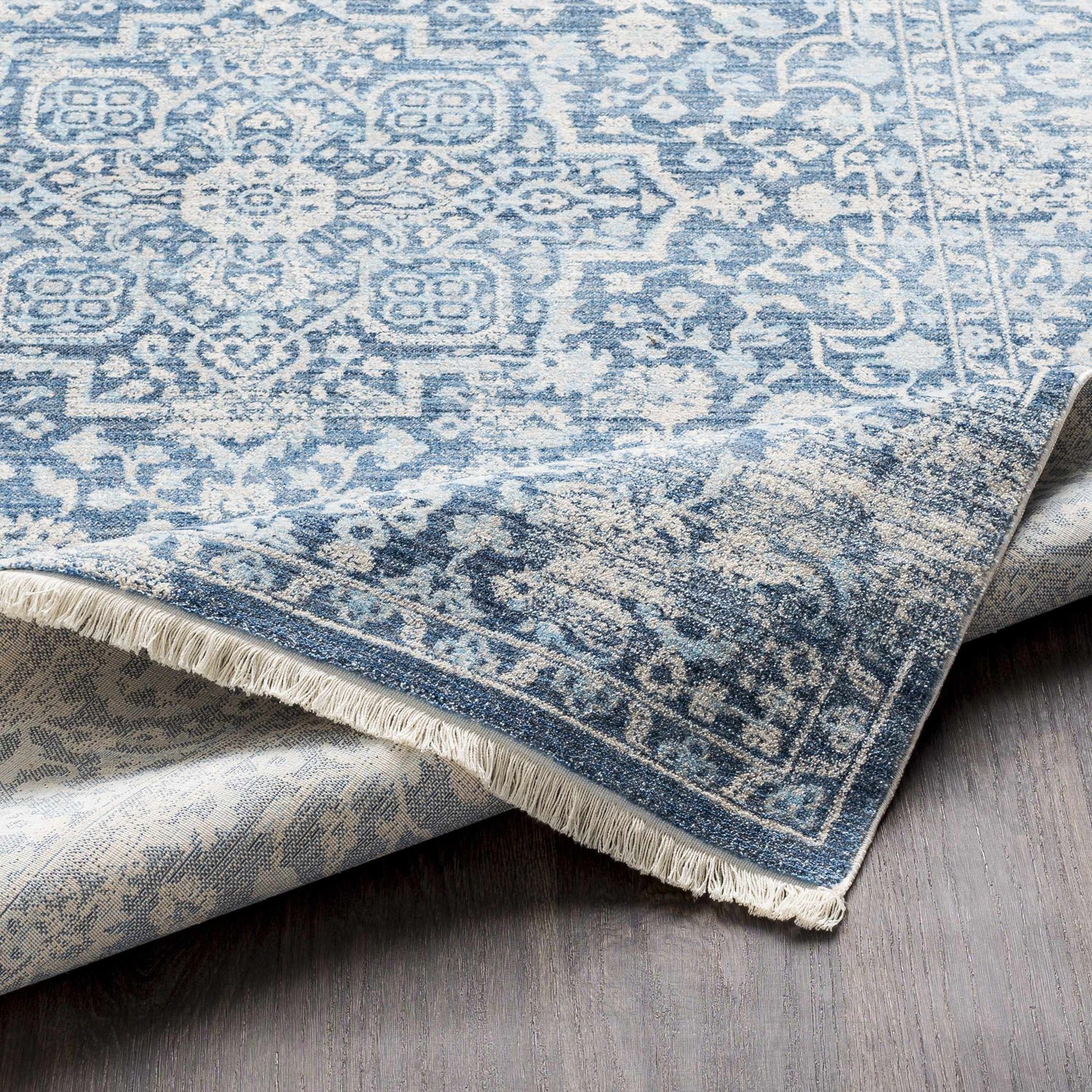Close-up of the Yorkana Distressed Blue Rug showing its traditional, vintage-inspired pattern and fringed edge. Fold
