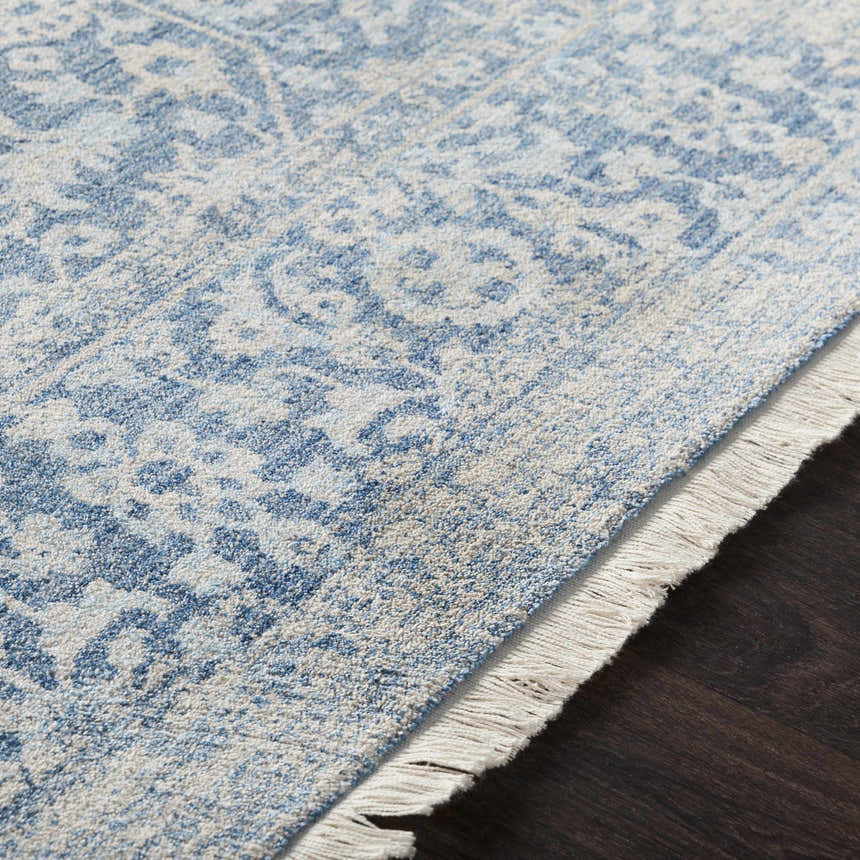 Close-up of the Yorkana Distressed Blue Rug showing its light blue, beige, and gray vintage-style pattern and fringe. Texture