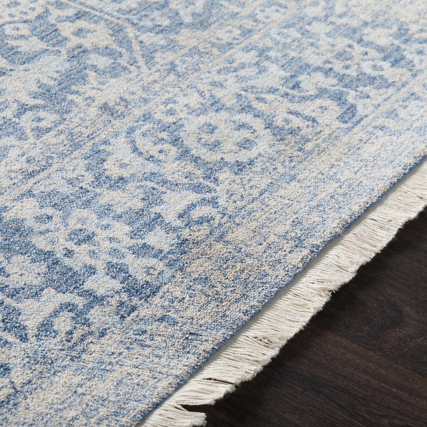 Close-up of the Yorkana Distressed Blue Rug showing its light blue, beige, and gray vintage-style pattern and fringe. Texture