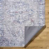 Close-up of Yoshi Washable Area Rug in denim, cream, and gray with a traditional pattern on a wood floor. Fold