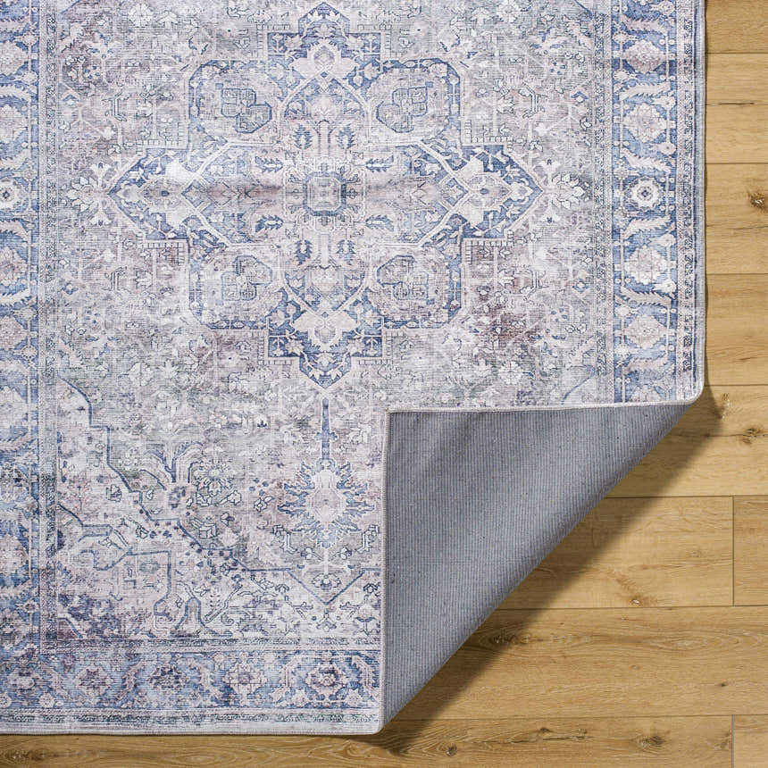 Close-up of Yoshi Washable Area Rug in denim, cream, and gray with a traditional pattern on a wood floor. Fold