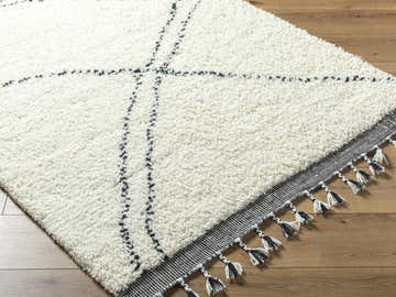 Close-up of the pearl Yumie Area Rug, a hand-woven wool rug with black geometric lines and tassels. Farmhouse style. Corner