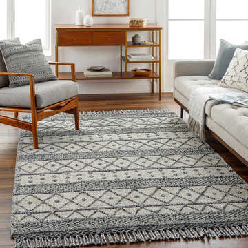 Living room scene with gray sofa and chair, showcasing the bone and dark gray Yuko Area Rug with a bohemian diamond pattern. Roomscene-Rectangle