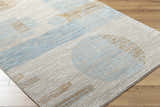 Close-up of the Yoite Area Rug. Contemporary design in blue, ivory, mustard, peach, and tan. Machine woven polyester rug. Corner