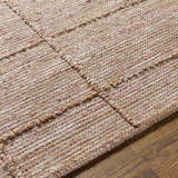 Close-up of the hand-woven Zana Area Rug showing its brown, tan, off-white, and burgundy color palette and textured jute blend. Texture