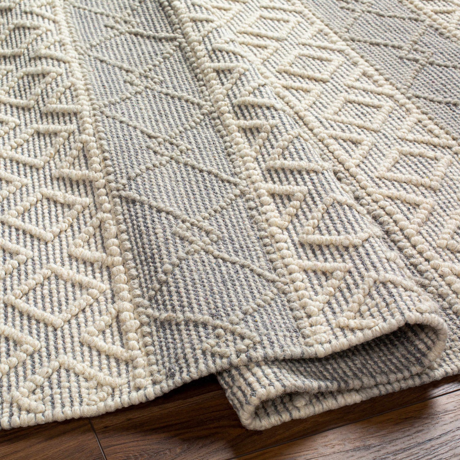 Close-up of Zaza Wool Rug in bone and cloud gray. Hand-woven geometric pattern with textured details. Fold