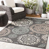 Outdoor patio scene with Zephyrhills Area Rug, wicker chair, side table, and potted plants. Roomscene-Rectangle